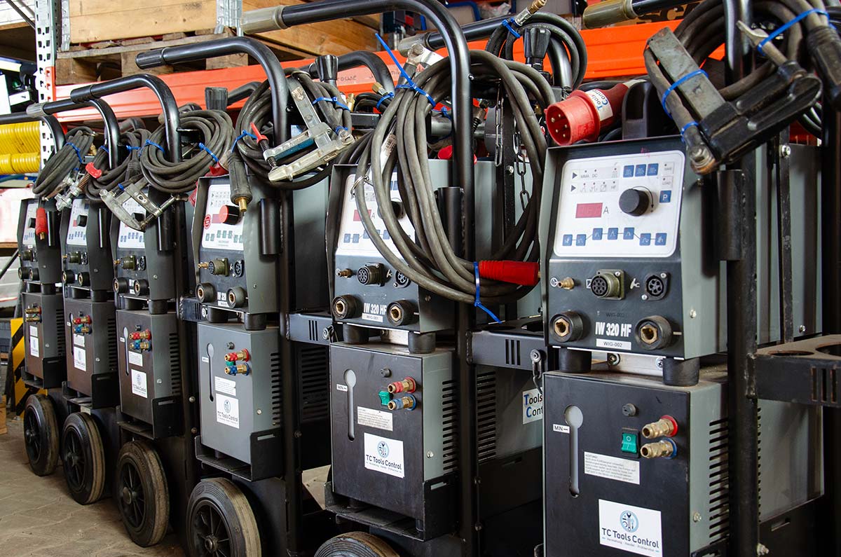 Reihe von mobilen Schweißgeräten mit angeschlossenen Kabeln und Handgriffen in einer Werkstatt.